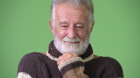 handsome senior bearded man wearing warm clothing against green background