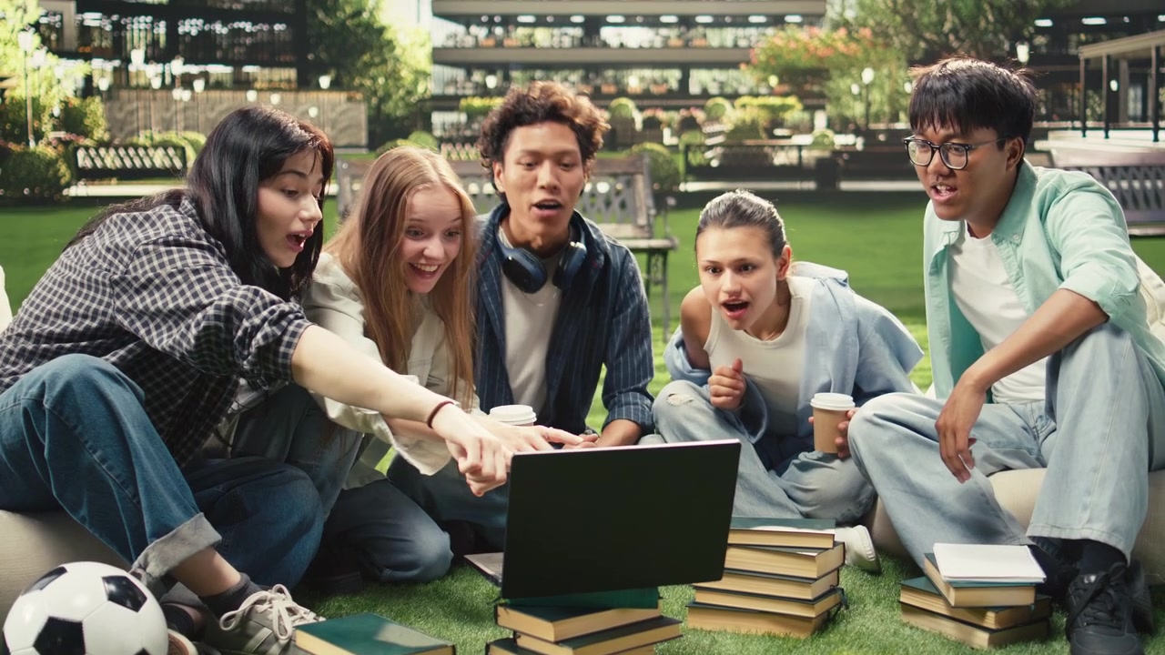 Diverse students checking notes on laptop with stack of books