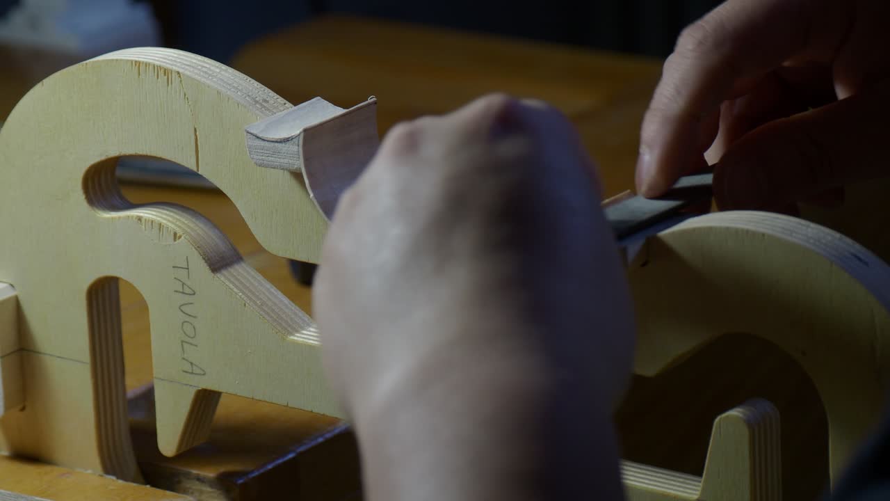 Luthier shaping violin or viola ribs on an internal mold, refining curves and edges around blocks using a small hand file to define the instrument body outline and structure, close up handheld sho
