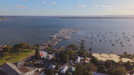 wide drone pass over belmont marina and open water showing sunset reflection and boat docks, panoramic aerial