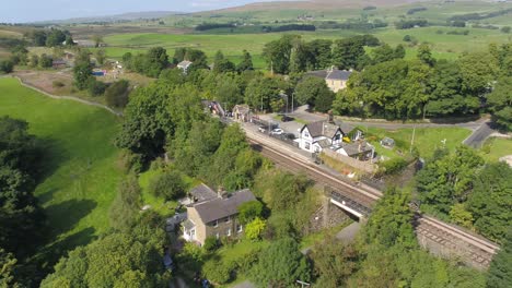 Imágenes-Aéreas-De-La-Estación-De-Tren-De-Clapham,-Línea-Ferroviaria,-Puente-Ferroviario-De-Piedra-Y-Río-En-La-Zona-Rural-De-Yorkshire,-Reino-Unido