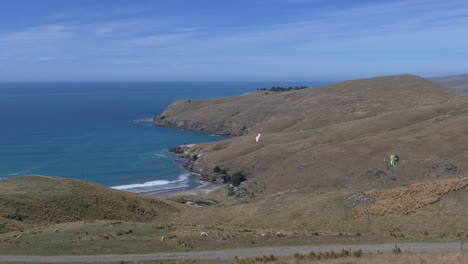 los parapentes se elevan sobre un paisaje árido en contraste con el hermoso océano azul en verano - cabeza de godley, península de los bancos
