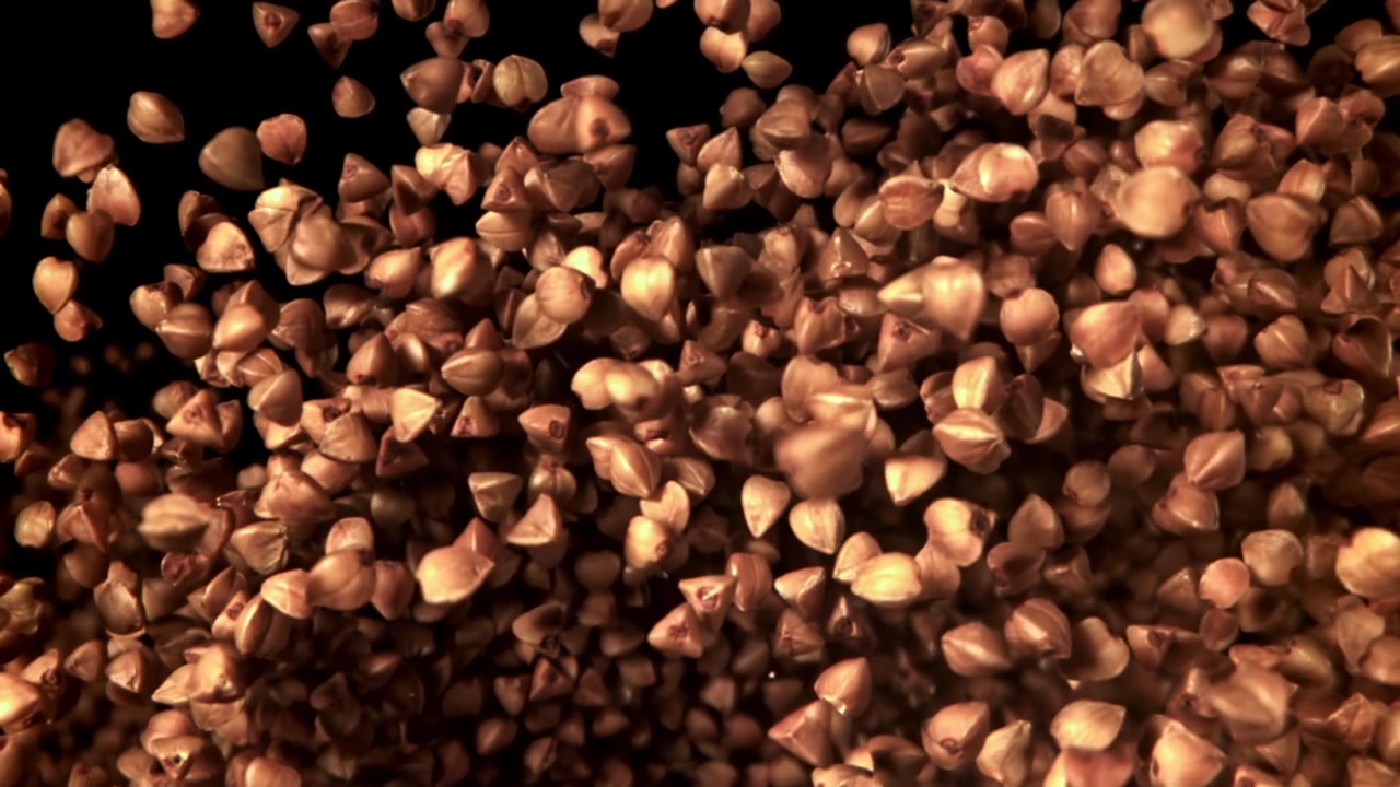 Raw Buckwheat Grains Falling in Slow Motion on Black Background