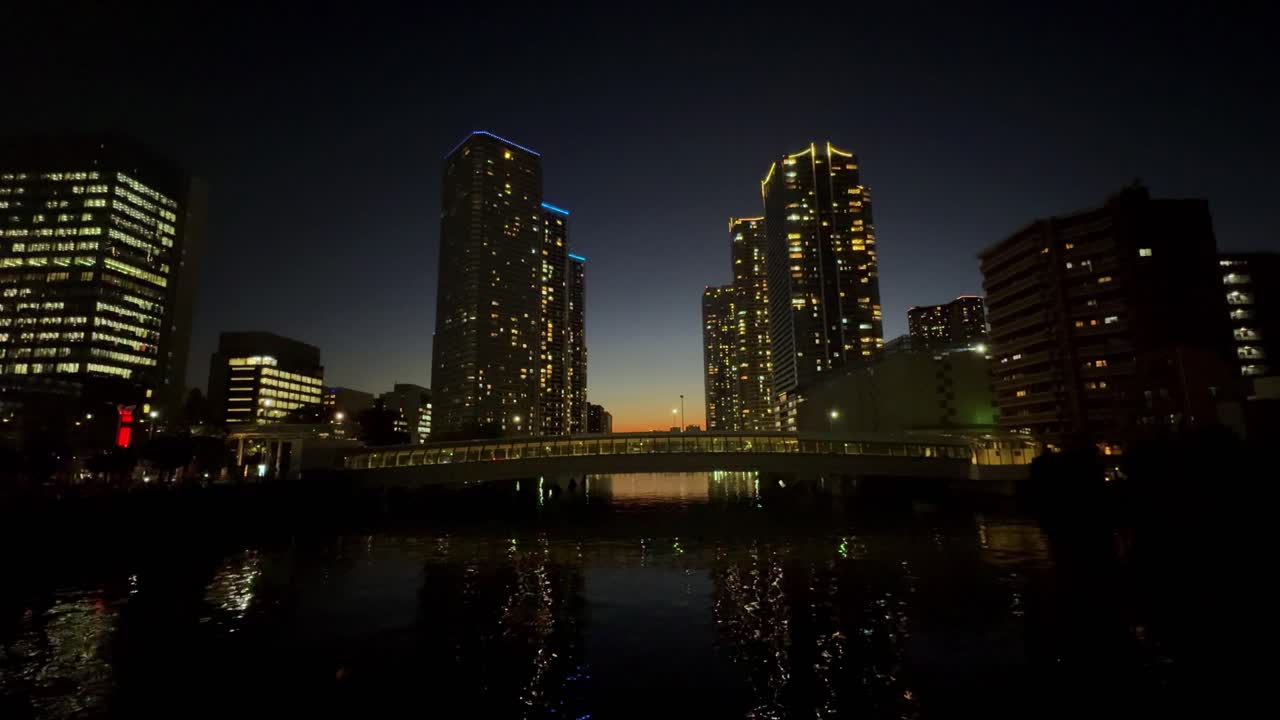 어두워지면서 조용한 물 위에 반사되는 조명된 도쿄 마천루의 놀라운 풍경