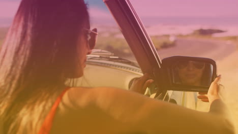 animation of light shade over biracial woman looking in car mirror at seaside
