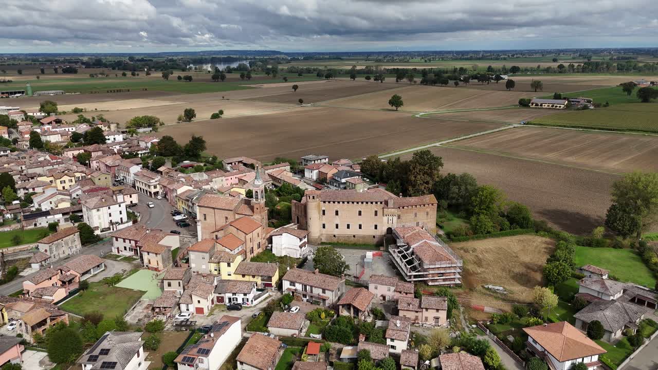 Carrellata aerea con drone sul villaggio di Calendasco, in provincia di Piacenza, che mostra il Castello medievale di Calendasco, la Chiesa di Santa Maria Assunta e la vasta campagna agricola della Pianura Padana.