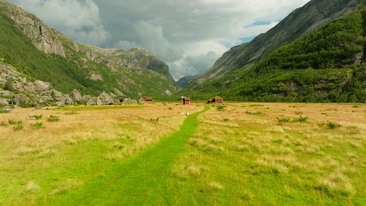 Norwegian mountain valley with cabins. Aerial forward at low altitude over green pastures