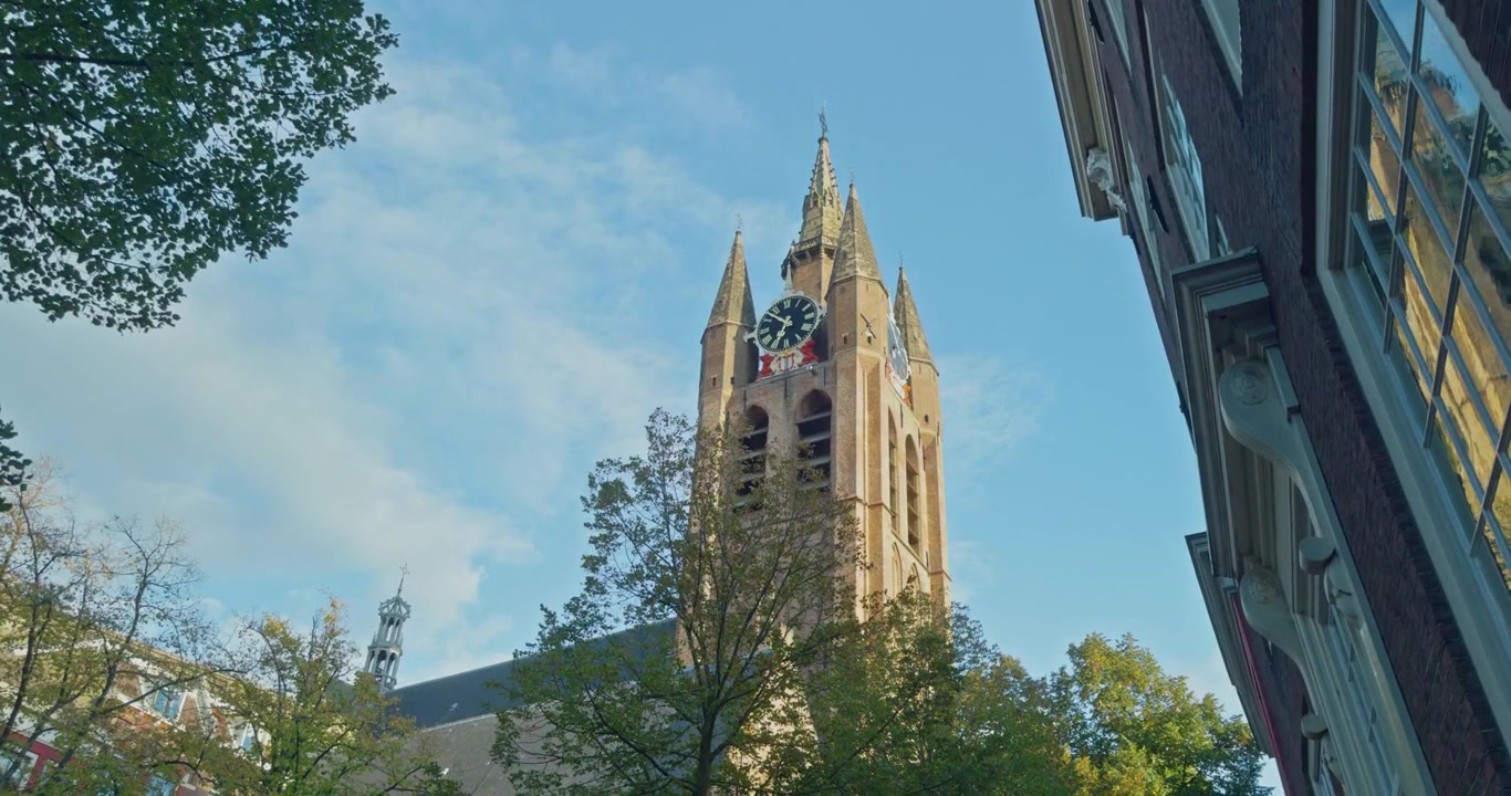 Paesi Bassi, Europa, torre di una cattedrale storica con guglia dell'orologio contro un cielo azzurro limpido con nuvole, circondata da alberi verdi e edifici in mattoni adiacenti, vista dell'architettura urbana