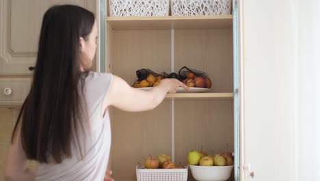 a woman of european appearance puts fruit in the kitchen cabinet useful and tasty fruits from your own garden a woman of european appearance puts fruit in the kitchen cabinet