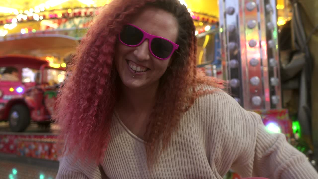 mujer con sonrisa y gafas de sol baila mirando a la cámara con el fondo de la feria detrás de ella