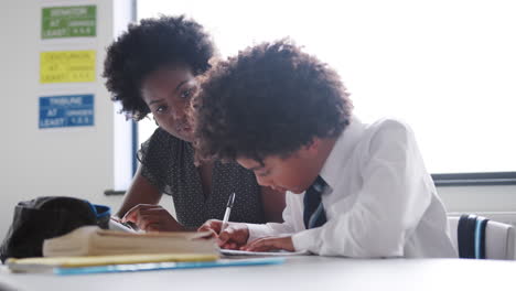 Weibliche-Gymnasiallehrerin-Mit-Digitalem-Tablet,-Die-Männlichen-Schülern-In-Uniform-Eins-Zu-Eins-Unterricht-Am-Schreibtisch-Gibt-Giving