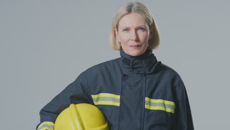 studio portrait of serious mature female firefighter against plain background