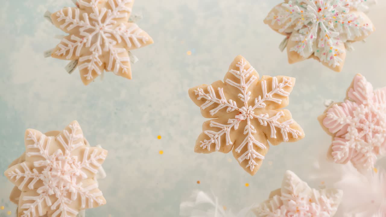 Falling gold flecks making central snowflake cookie bobbing on pale blue backdrop with pink cookie