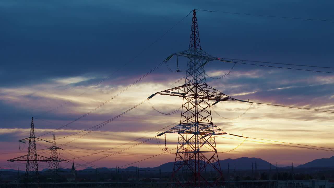 Power lines and electrical towers stand in a rural area as the sun sets showcasing energy