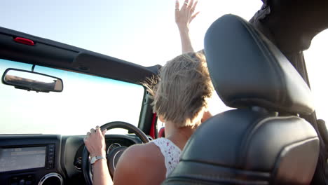 a young caucasian woman enjoys a drive in a convertible on a road trip