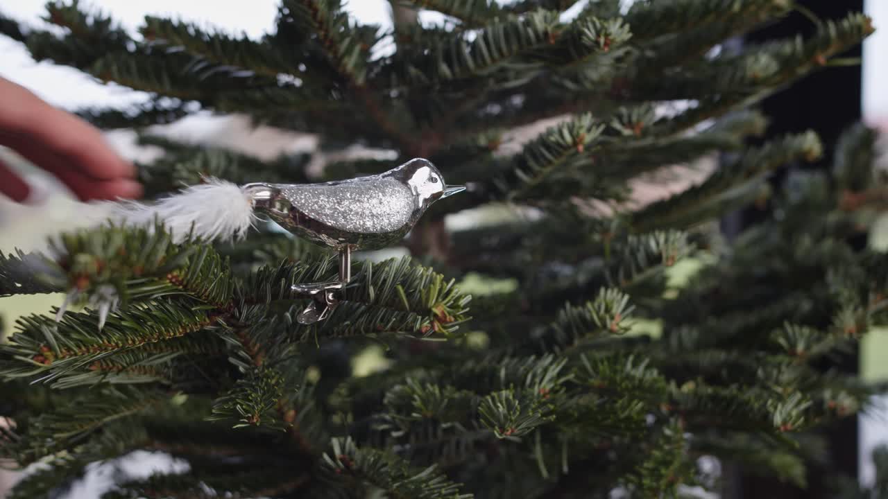 Hängender eleganter Silbervogel mit weißem Schwanzschmuck am grünen Weihnachtsbaum.