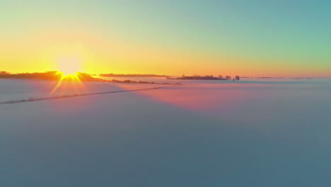 glowing golden sunset on the horizon of an empty snowy landscape of rural farmland fields - aerial view