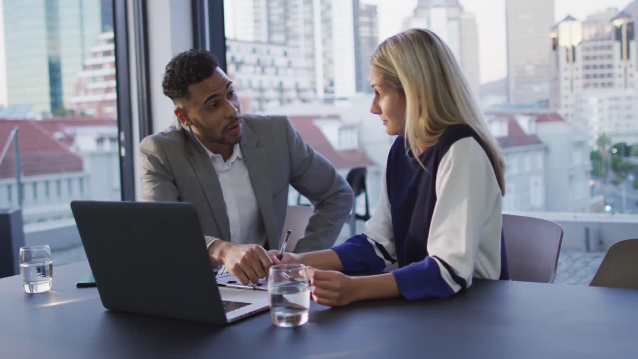 Video of two diverse male and female colleagues discussing and using laptop in office