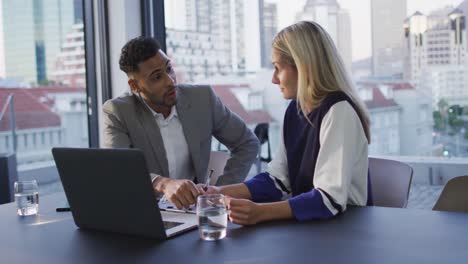 Video-of-two-diverse-male-and-female-colleagues-discussing-and-using-laptop-in-office