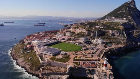 green stadium of gibraltar national rugby union team at europa point with the recognizable lighthouse above the high cliffs and rocks where the waves crash on a sunny day