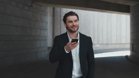 smiling business man recording voice message on cellphone in modern city