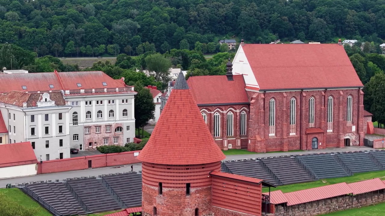 Video drone rivela la Città Vecchia di Kaunas e l'iconico Castello di Kaunas, evidenziando torri medievali in mattoni, edifici storici, paesaggio verde e la drammatica luce estiva in un'ampia inquadratura grandangolare