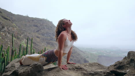 Seated-at-a-cliff's-edge,-the-woman-assumes-a-dog-pose,-facing-the-ocean,-inhaling-the-sea-breeze-during-her-yoga-journey-across-the-islands