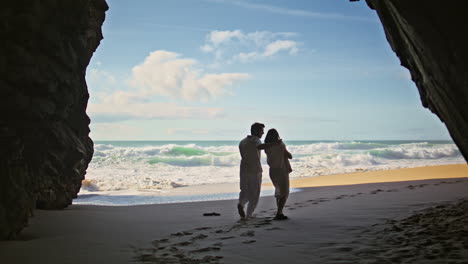 back view couple walking coast from rock shadow. spouses stepping on golden sand