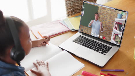 chica afroamericana usando una computadora portátil para una lección en línea con un profesor caucásico en la pantalla