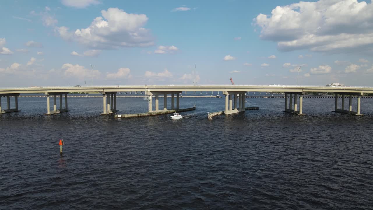 A boat passes beneath the Green Bridge in Bradenton, Florida, with cars traveling above. Crane Down