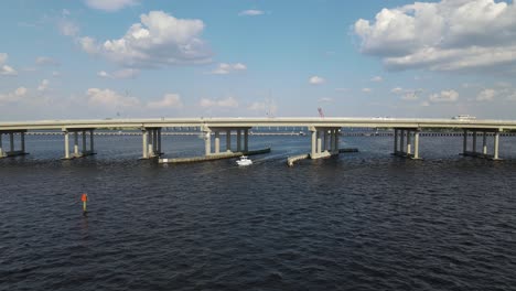 a boat passes beneath the green bridge in bradenton, florida, with cars traveling above. crane down