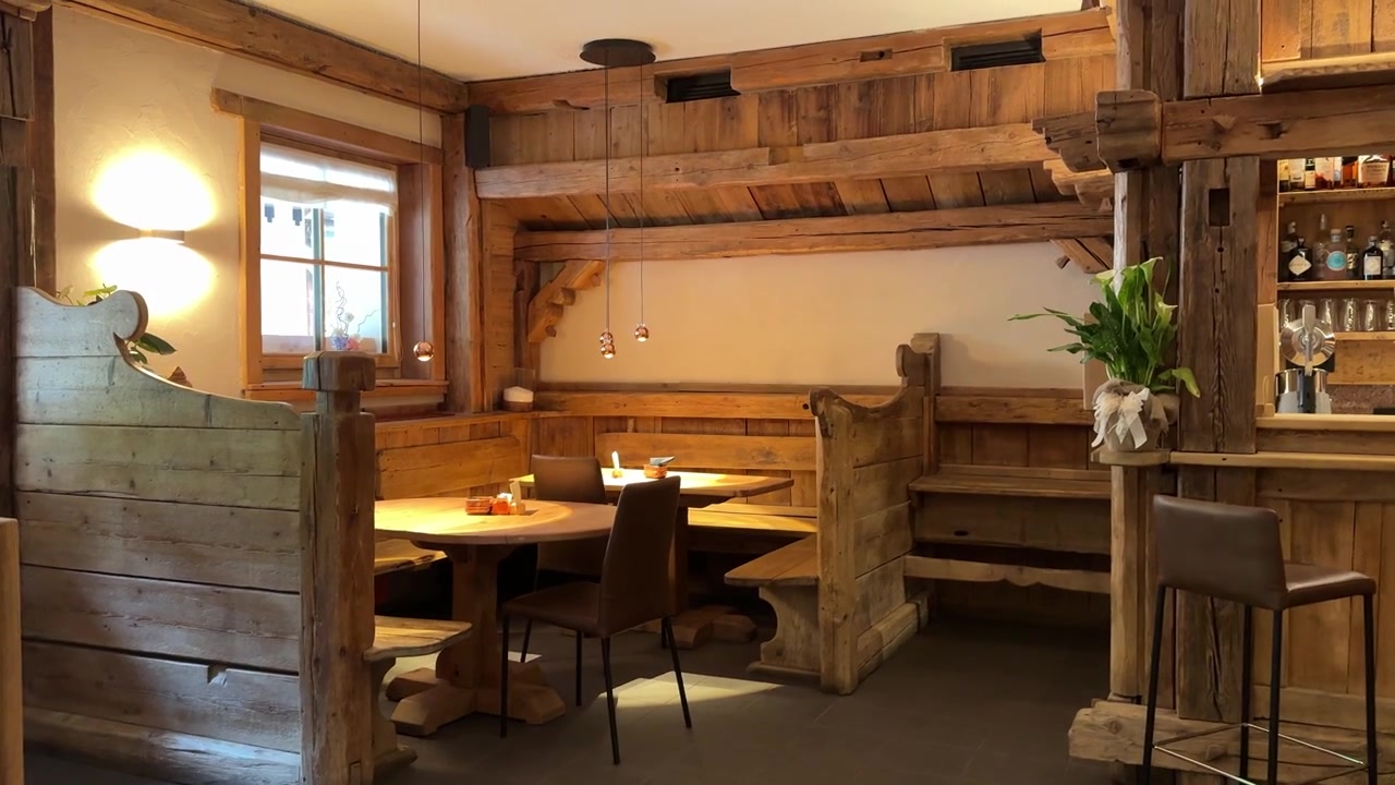Interno accogliente di un ristorante in legno all'interno di un tradizionale rifugio di montagna delle Dolomiti, caratterizzato da mobili rustici, illuminazione calda e un'atmosfera di ospitalità alpina.