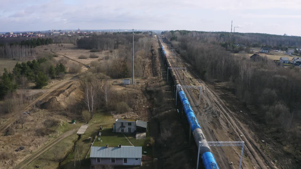Trasportation scene of industrial train with many tank wagons is passing rural area, leafless trees alongside the railway - aerial drone