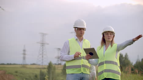 un grupo de ingenieros en una central eléctrica de alto voltaje con una tableta y dibujos caminan y discuten un plan para el suministro de electricidad a la ciudad.