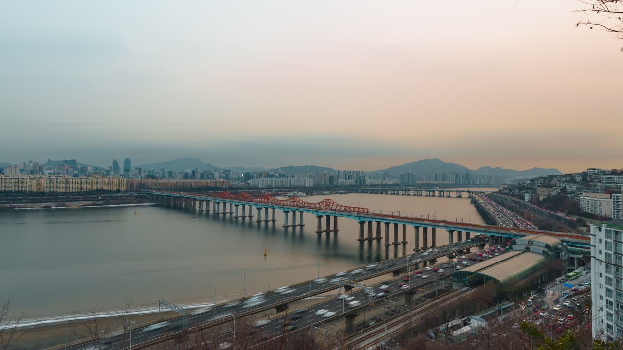 Hyperlapse con zoom indietro del traffico intenso sulla superstrada Gangbyeonbuk-ro, Ponte Donho sul fiume Han, skyline di Gangnam e Hannam, montagne, tramonto invernale caldo e nebbioso sulla città di Seoul.