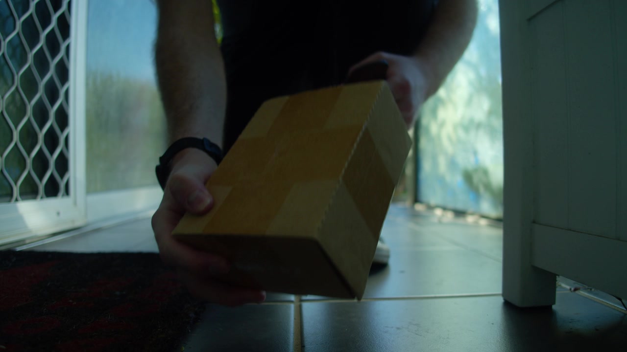 Ripresa cinematografica in 4K di un giovane che ritira un pacco dalla sua veranda prima di aprire la porta d'ingresso e portare la consegna all'interno della sua casa