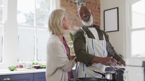 caucasian senior woman tying apron to her husband in the kitchen at home