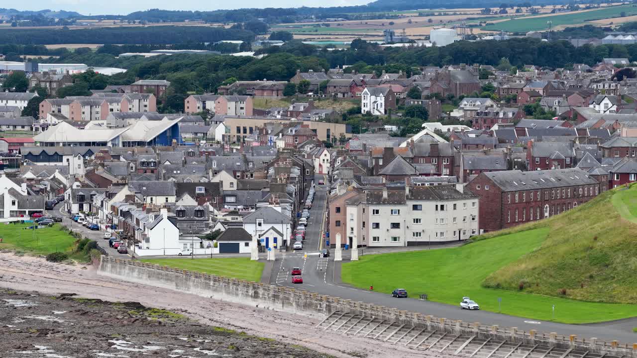Wide daytime aerial pan reveals historic coastal town architecture, rooftops, and streetscape in overcast light
