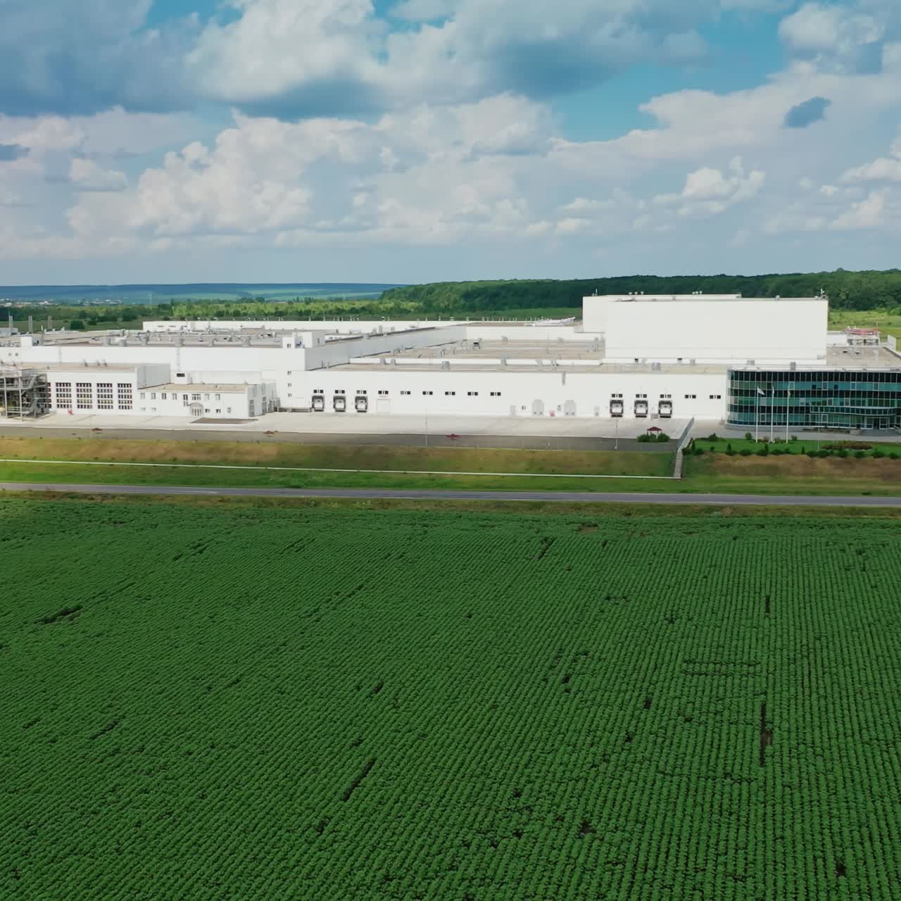 Modern industrial plant in green fields. Large territory of innovative factory among green nature in summer. Aerial view. Camera moves to the right.