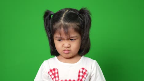 portrait of asian angry and sad little girl on green screen background, the emotion of a child when tantrum and mad, expression grumpy emotion. kid emotional control concept