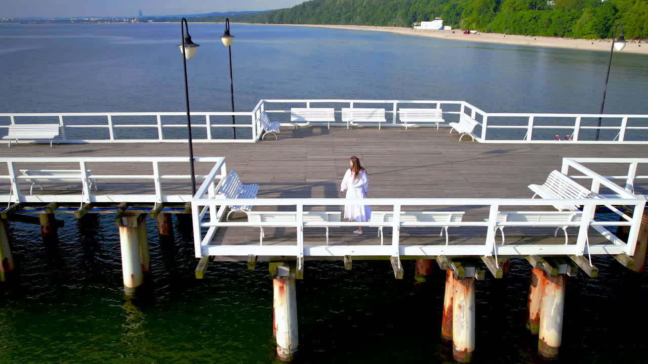 молодая женщина в белом платье наблюдает живописный морской пейзаж, гуляя по пирсу орлово, гдиния, польша, аэрофотосъемка