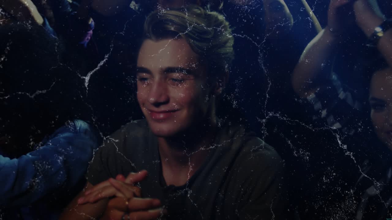 Man at center responding to music, clapping and handling smartphone under blue stage lights