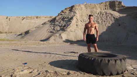 muscle athlete strongman man hits a hammer on a huge wheel in the sandy mountains in slow motion. strength and endurance training for wrestlers