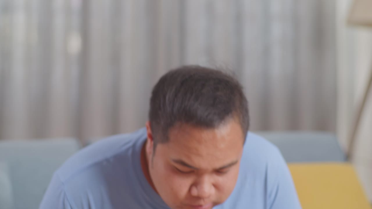 한 아시아 남자가 집에서 거실에서 긴 을 먹는 패스트푸드를 먹으면서 몸무게를 측정하고 있습니다.