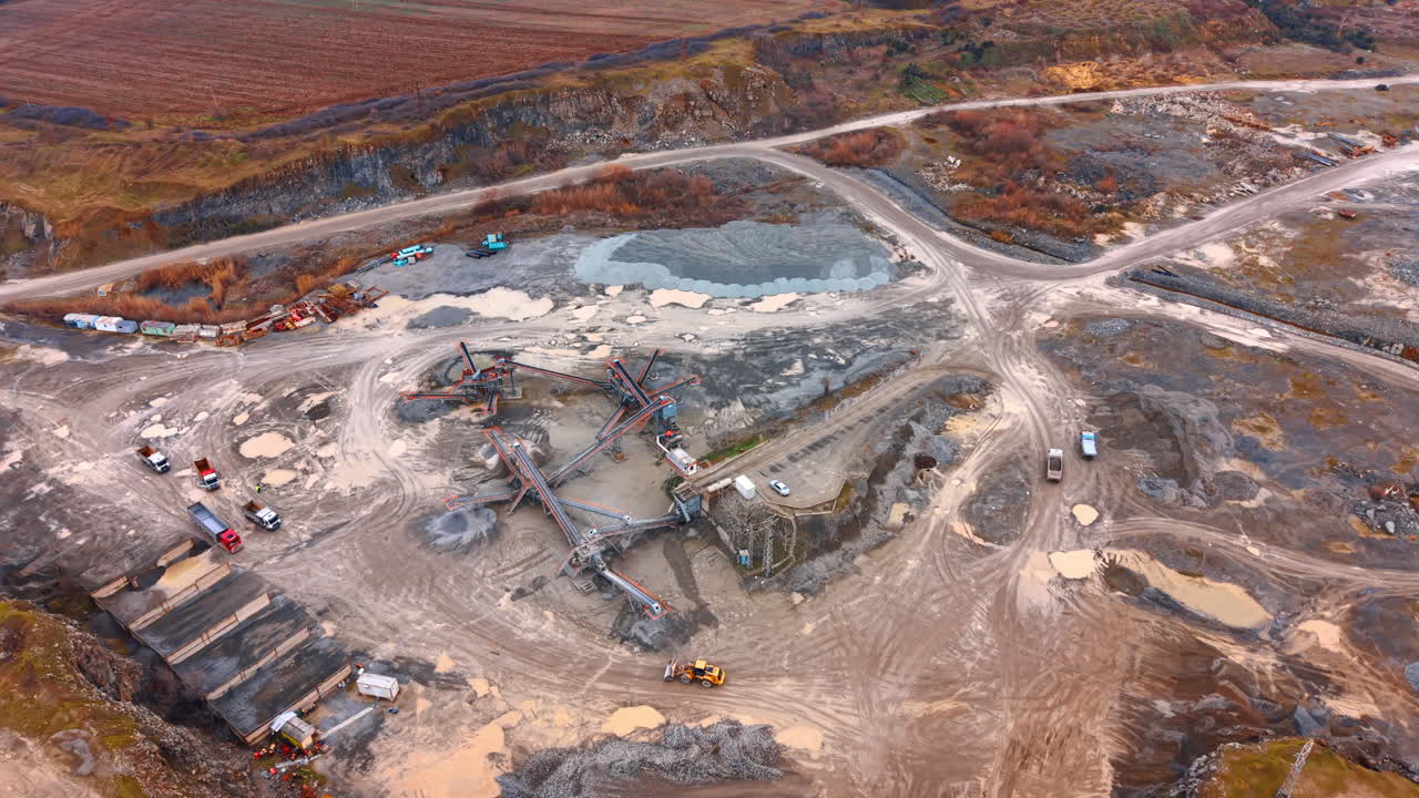 Rocky construction site with vehicles. Heavy machinery and trucks work on a construction site surrounded by hills