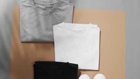 video of flat lay of multi coloured t shirts with copy space on brown and grey background