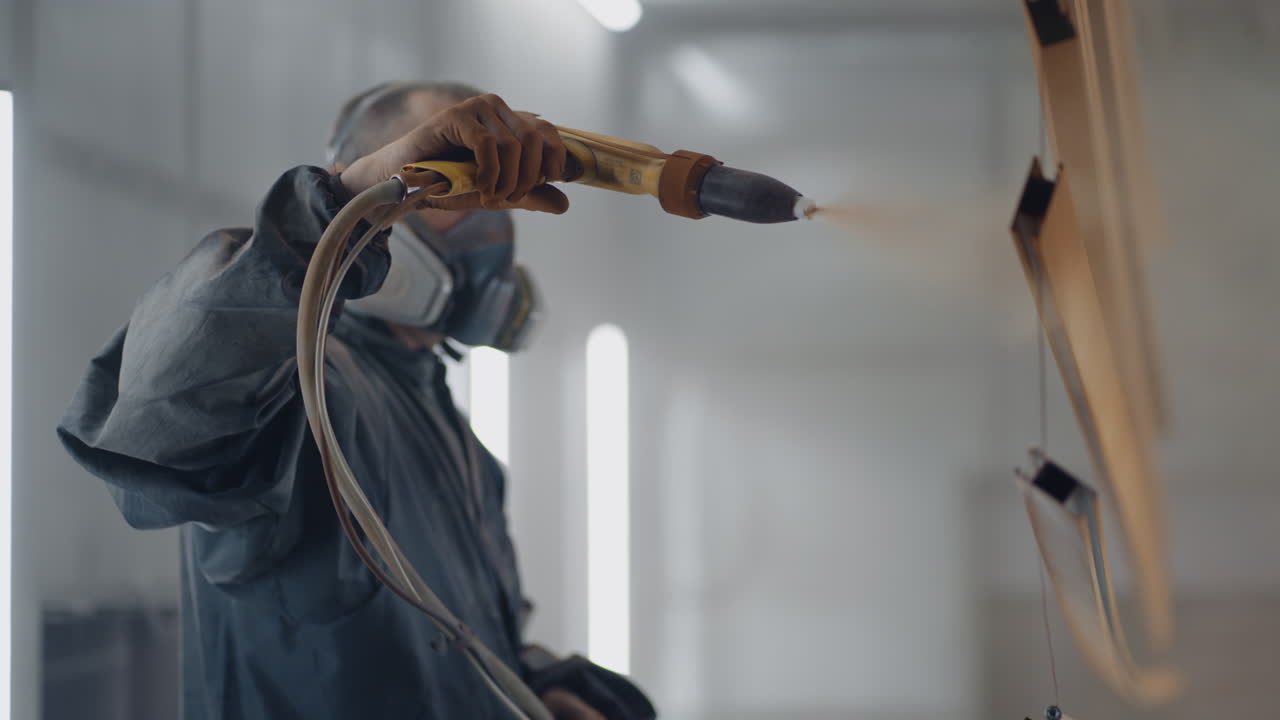 슬로우 모션에서 호흡기 마스크와 보호복의 강철 프로필에 몰라 스프레이 페인트. 생산 및 페인팅 스튜디오. 파우더 코팅