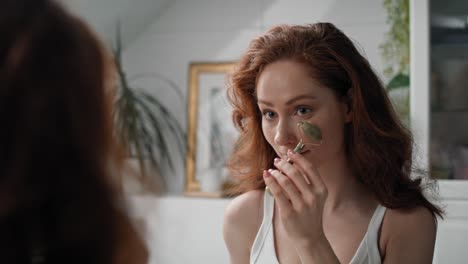 joven mujer caucásica usando un rodillo facial en el baño.