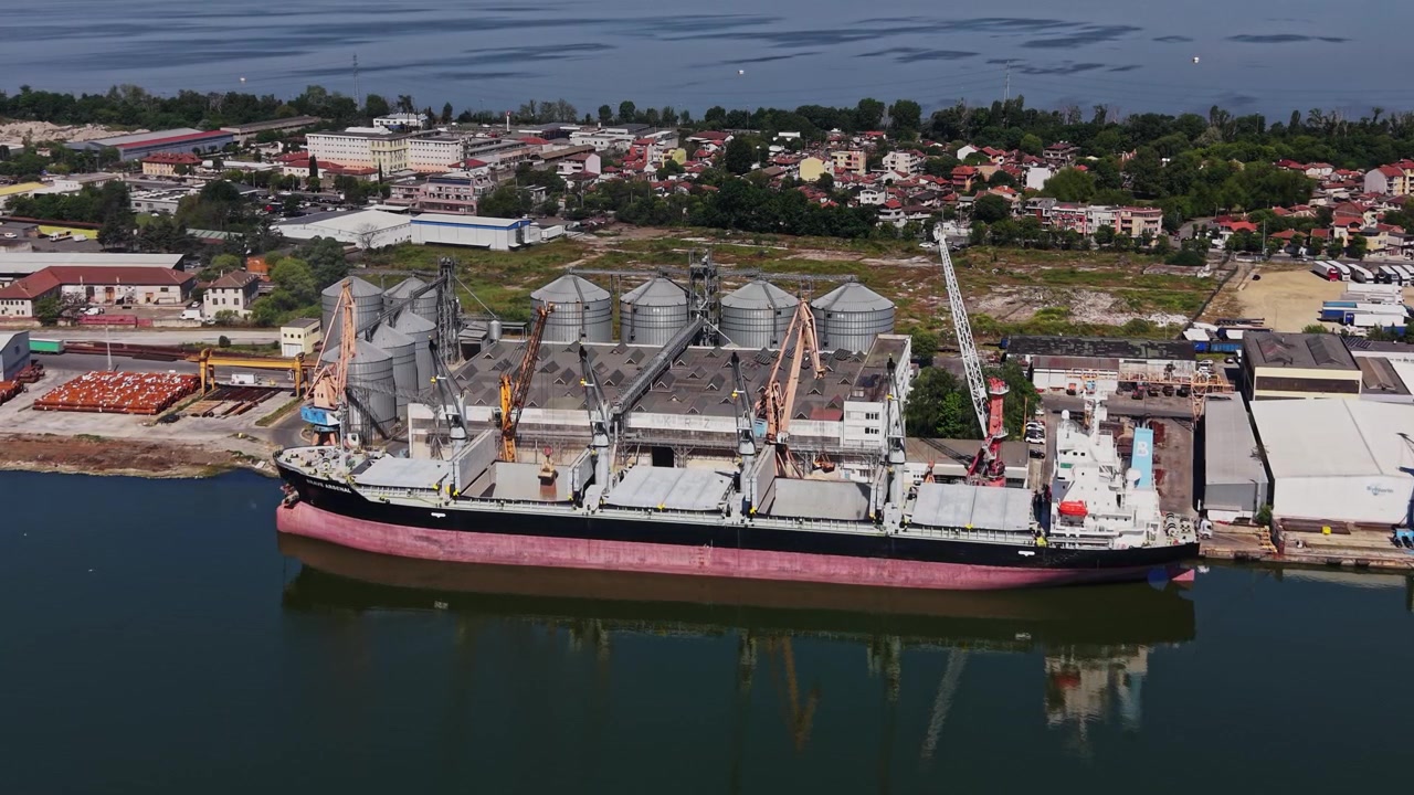 Buque de carga atraca en un puerto cerca de silos de almacenamiento en una zona costera.