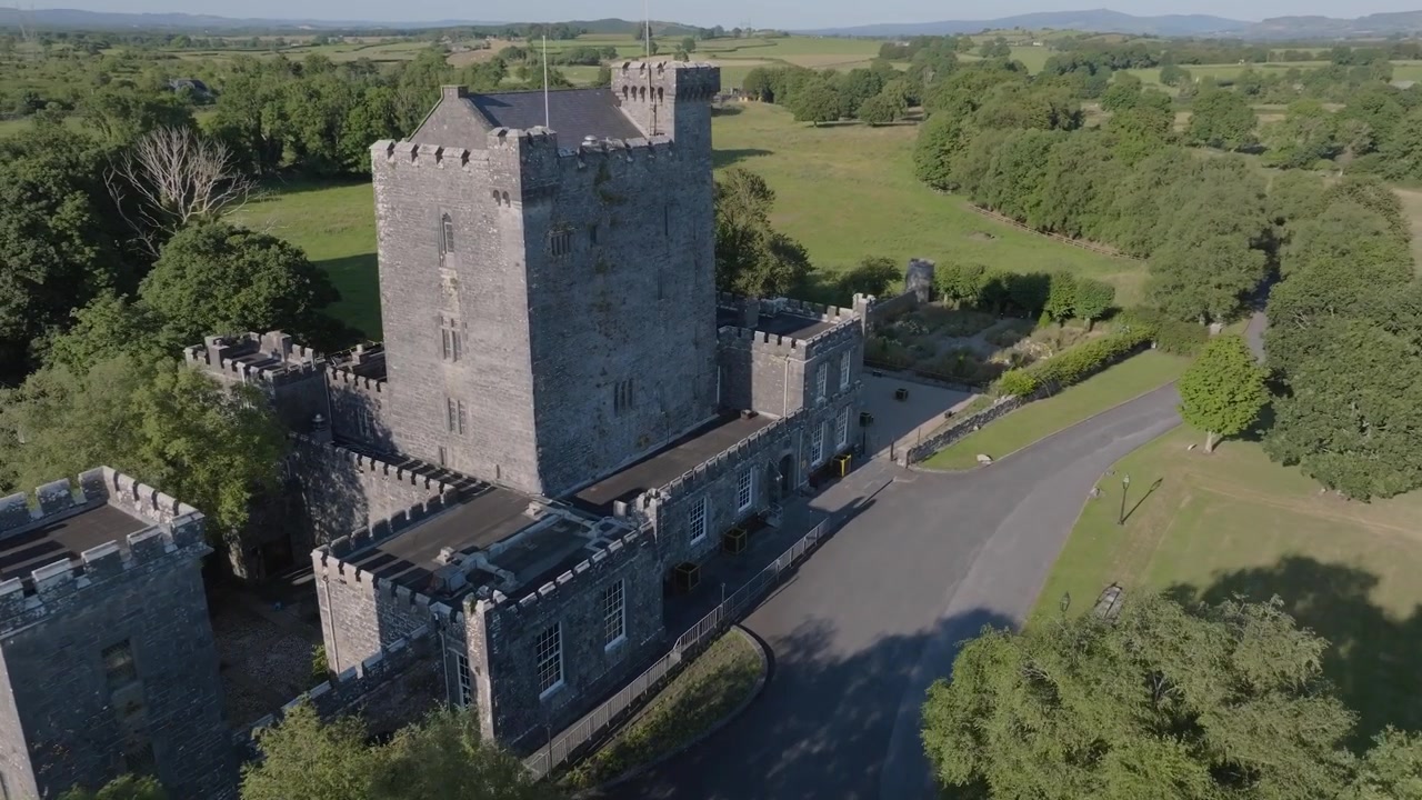 Complesso di un castello medievale irlandese si trova accanto a un vialetto pavimentato vuoto in mezzo alla campagna aperta, mentre il drone ne segue le mura.